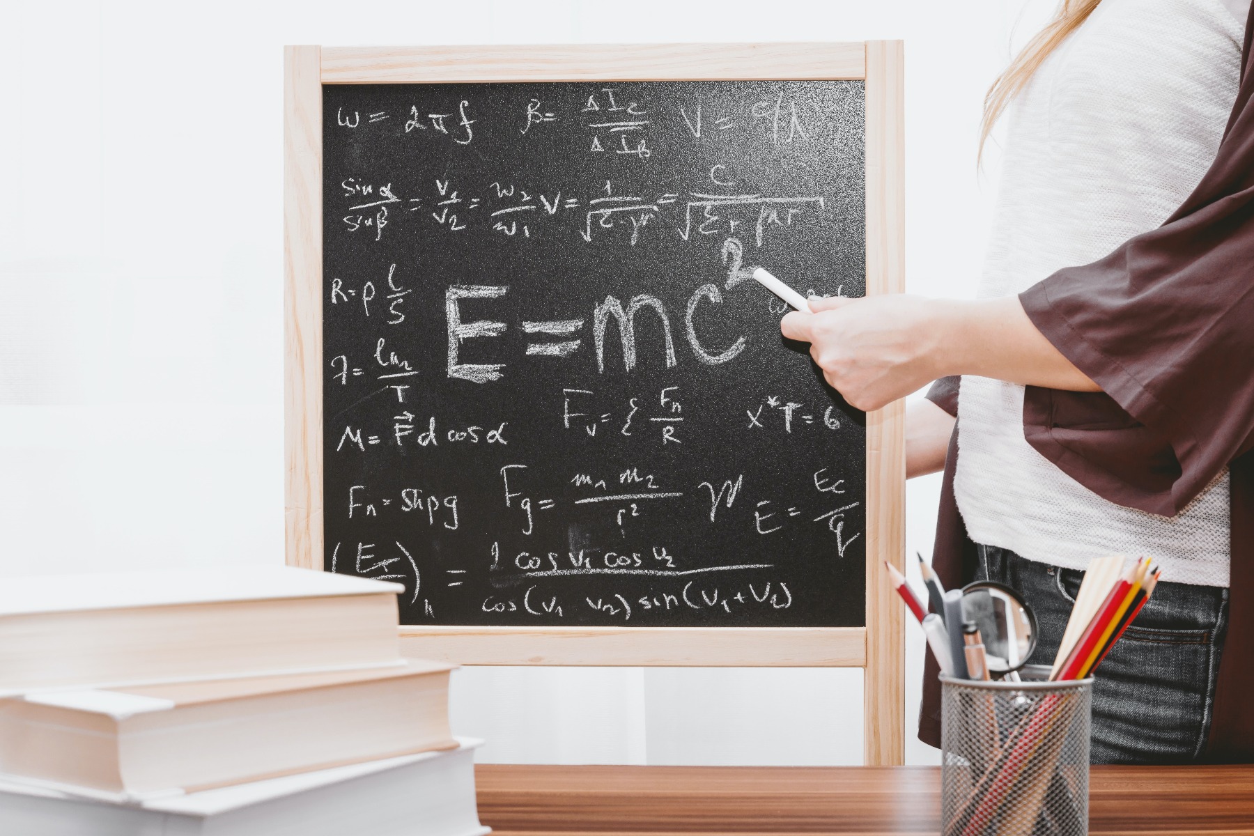 Woman pointing a piece of chalk to a chalkboard with math and an Einstein equation on it in a homeschool classroom.