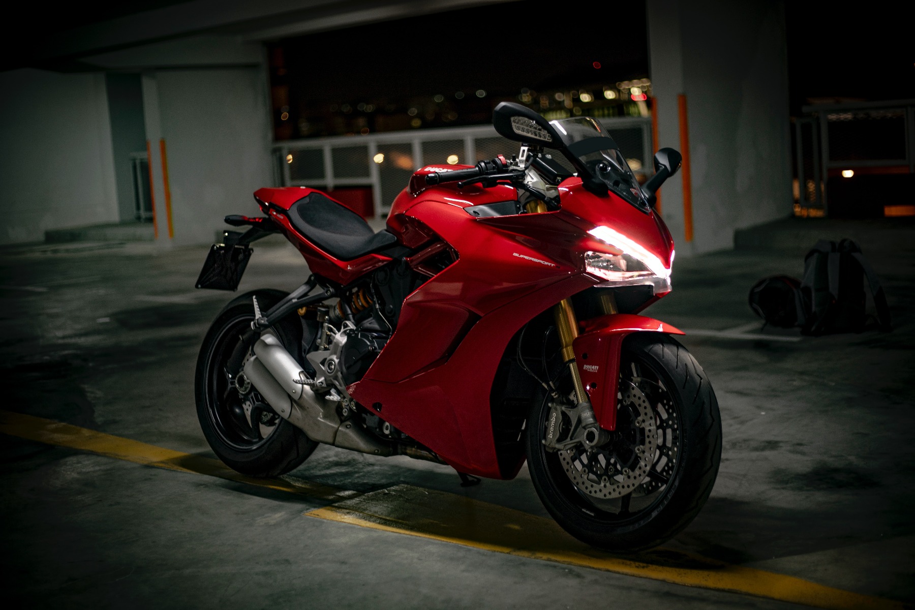 A red and black motorcycle sits in a parking garage at night.