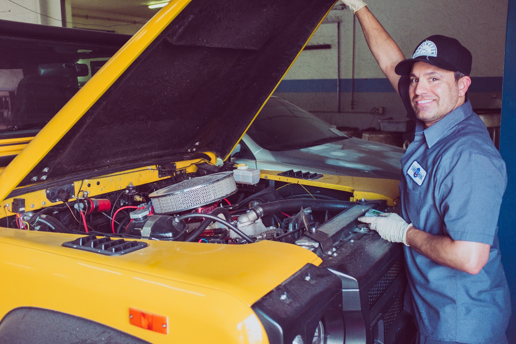 A mechanic works under the hood of a car using heat shrink tubing to combine wires.