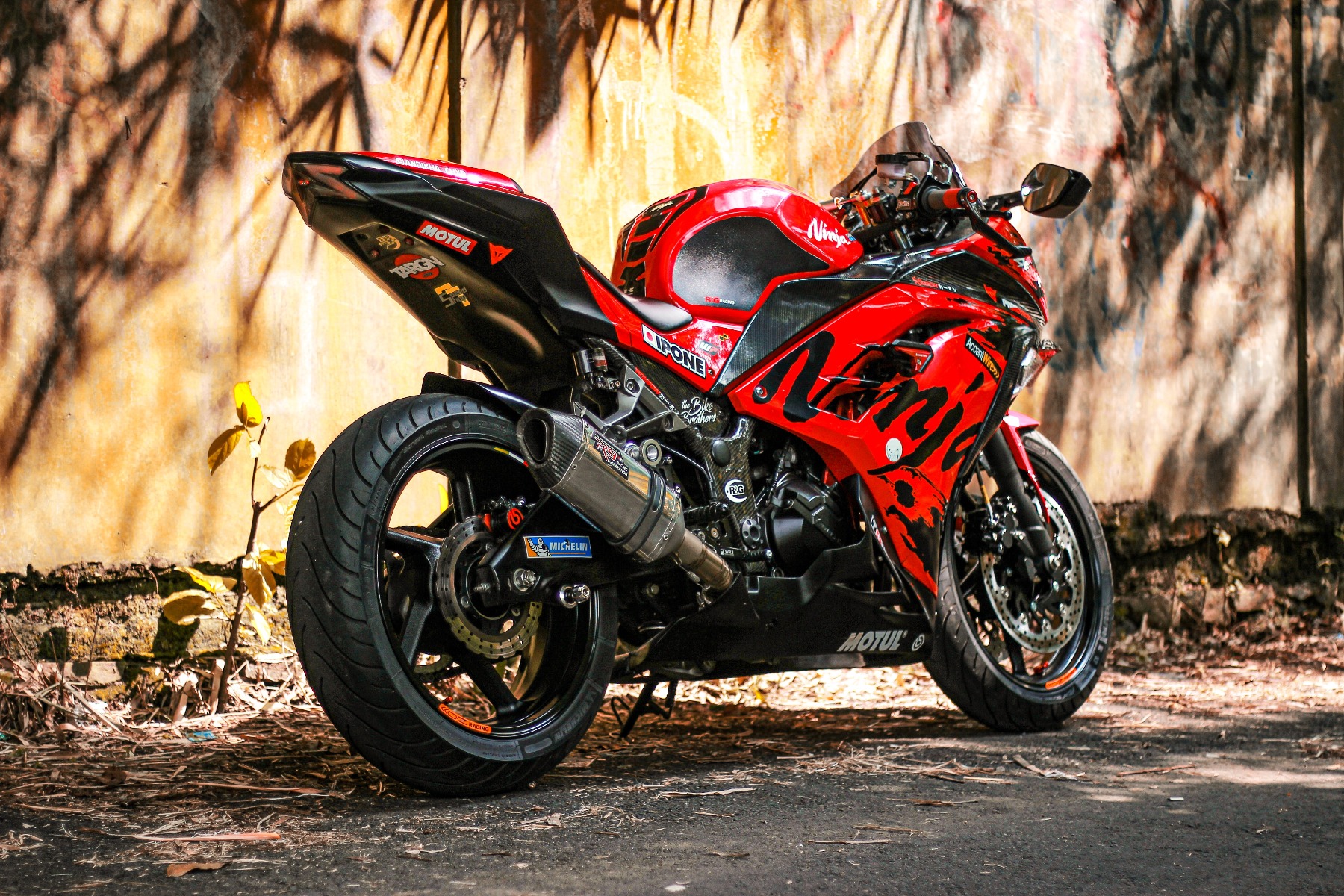 A red and black motorcycle is parked at the side of a building in the sunlight